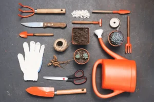 A collection of essential garden gadgets, including a watering can, gloves, trowels, scissors, and small pots, arranged neatly on a dark surface.