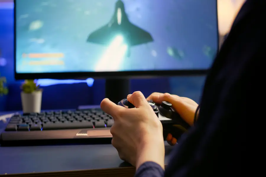 Person playing a space shooter game using a wireless controller on HSSGameStick setup with a monitor and keyboard.